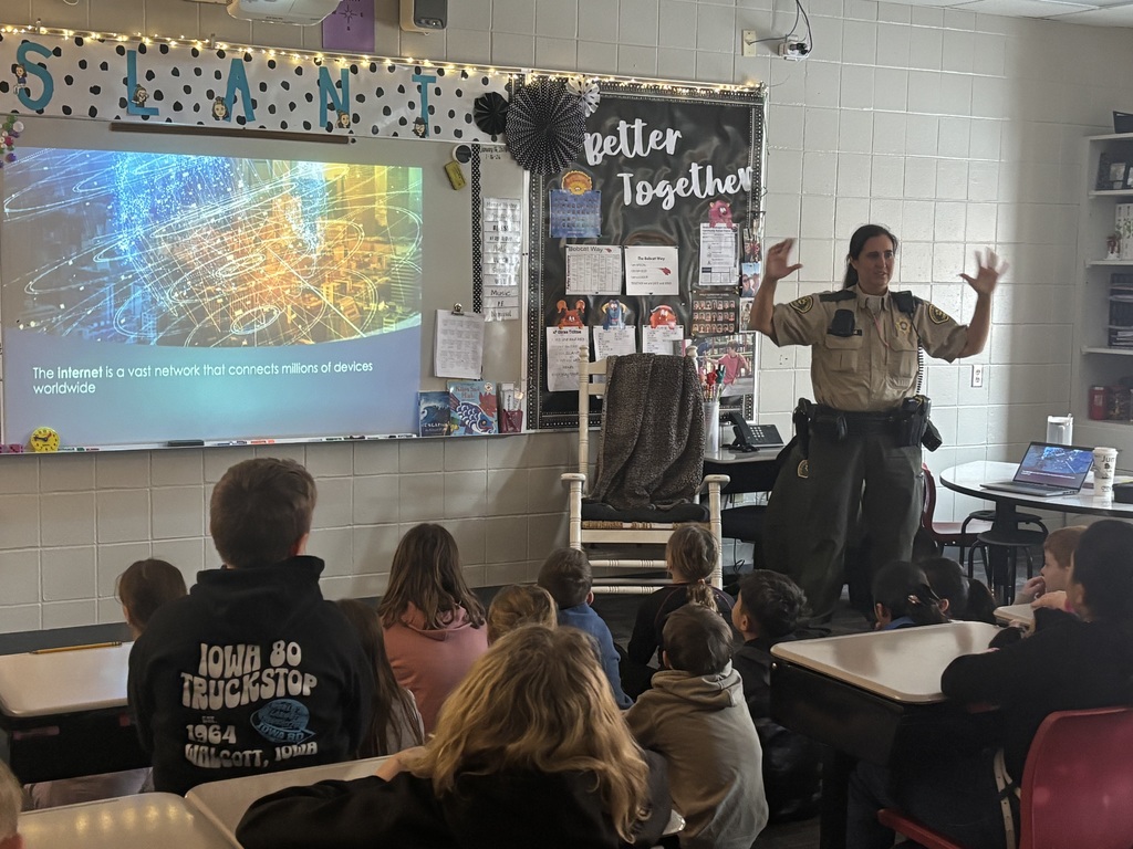 An officer gives a presentation to attentive students seated on the floor and at desks, with a slide reading, “The Internet is a vast network that connects millions of devices worldwide.”