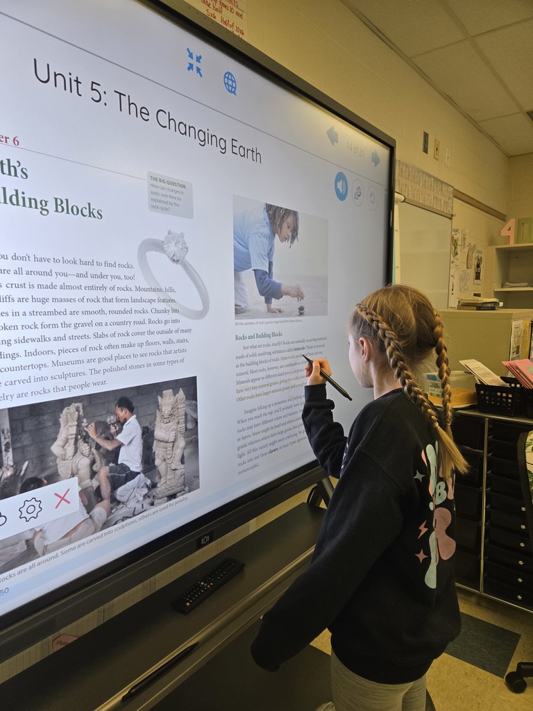 A girl with pigtail braids highlights content on a digital smartboard for a science lesson titled “The Changing Earth.”