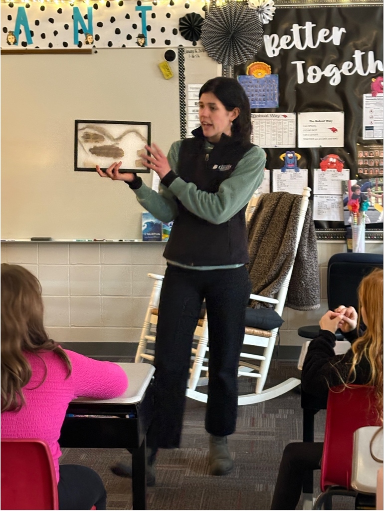 A presenter holds a framed display of animal tracks while students watch and listen.