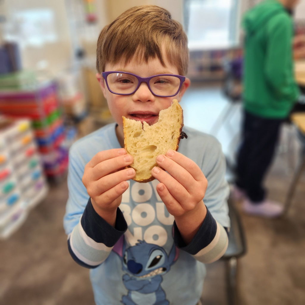 Student smiles and holds up a piece of bread in a classroom.
