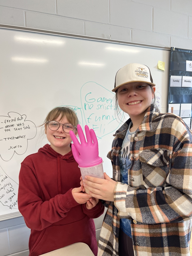 Two students smile and hold a container with a pink glove inflated on top.
