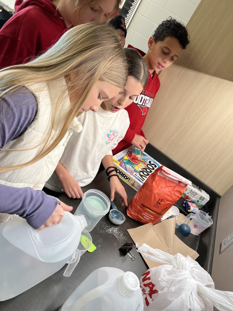 Students measure and mix ingredients at a counter for a classroom project.