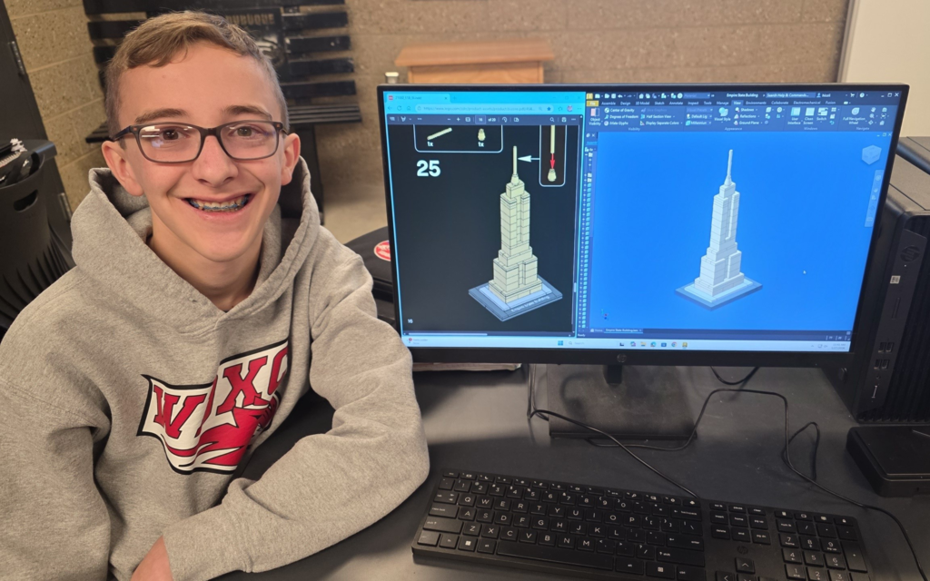 Smiling student sits at a computer displaying a 3D model of the Empire State Building.