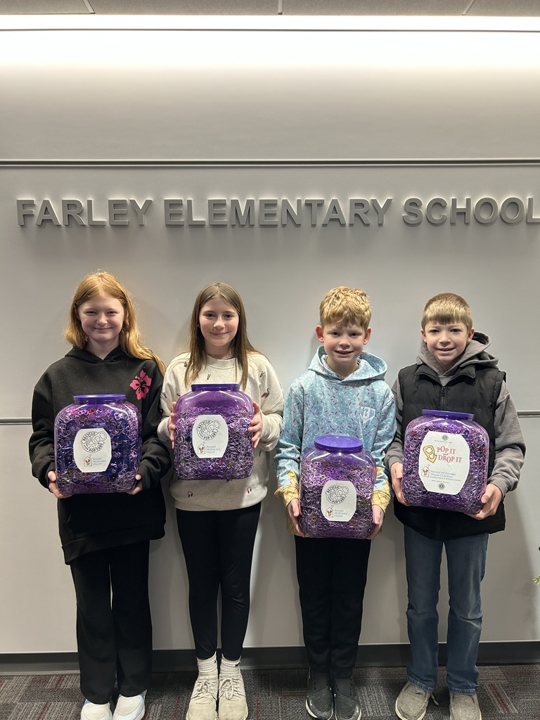 Four students stand in front of a “Farley Elementary School” sign holding large jars filled with purple pop tabs for the “Pop It Drop It” collection.
