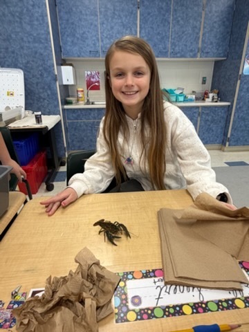 Student smiling while sitting next to a crayfish on the desk.