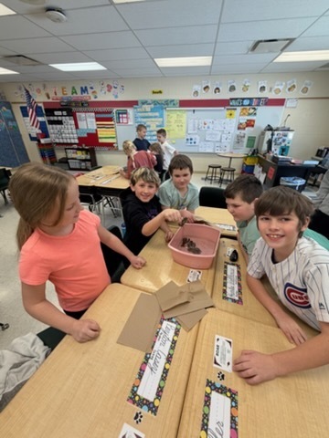 Group of students smiling around a table while observing a crayfish in a pink container.
