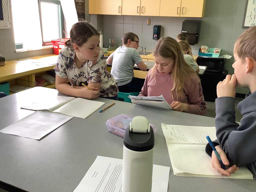 A small group of students collaborating on a reading or writing task at a classroom table.
