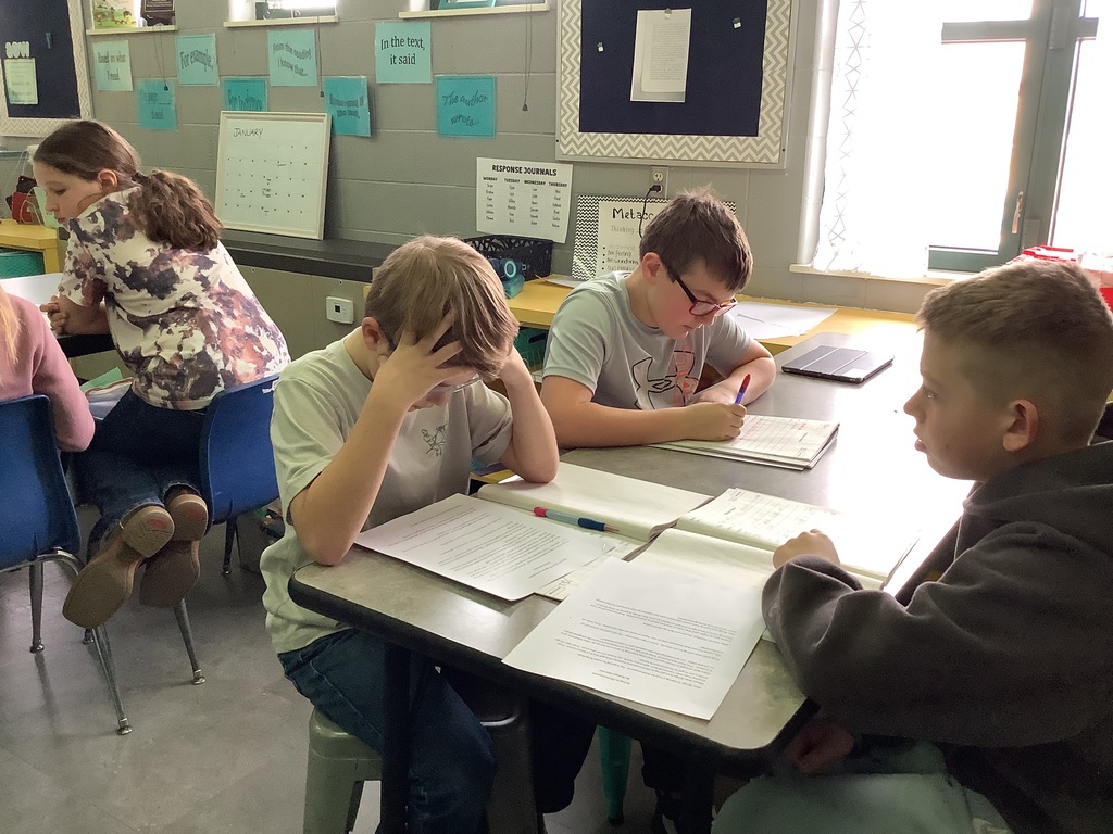 Three boys working together at a table, focused on their writing and assignments.
