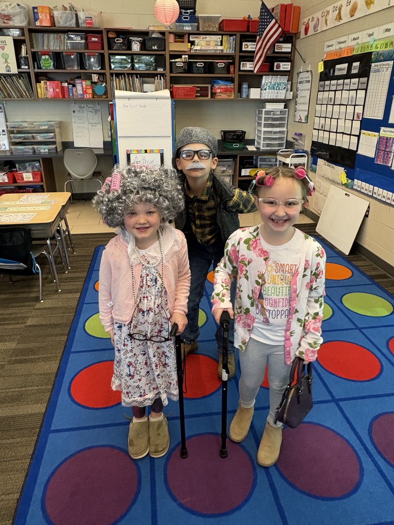 Three children in a classroom dressed as seniors, smiling and posing together.