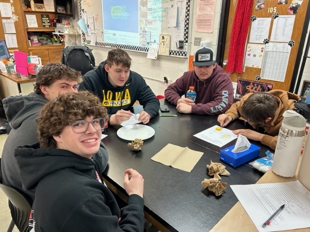 Group of students sit around a table examining an egg during a classroom activity.