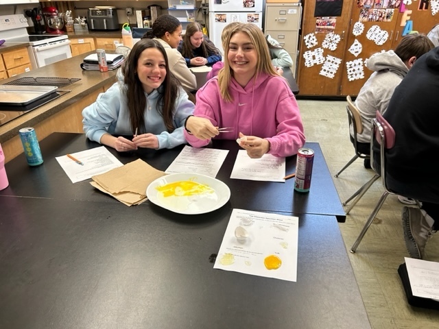Two students smile while separating egg yolks and working on a worksheet.