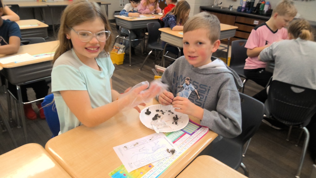A pair of students examine contents on a plate and worksheet during a hands-on activity.