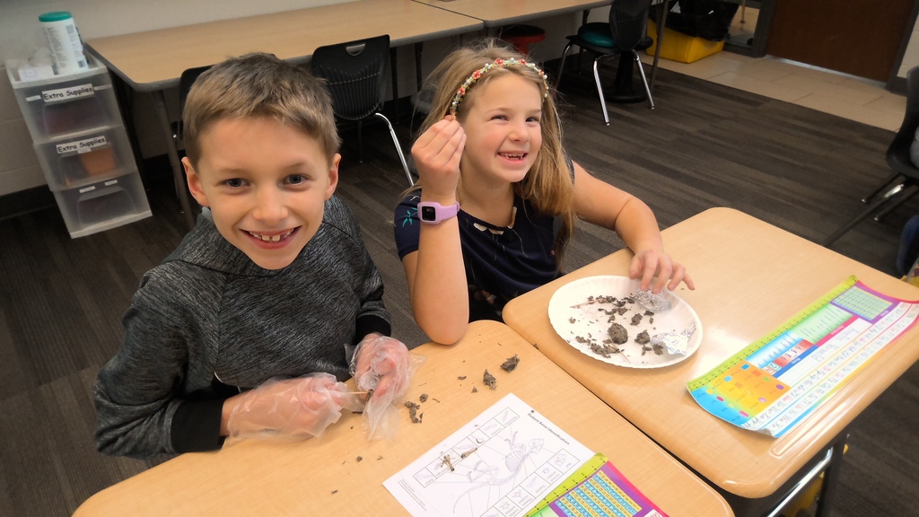 Two students grin while examining pieces on a plate for a classroom activity.