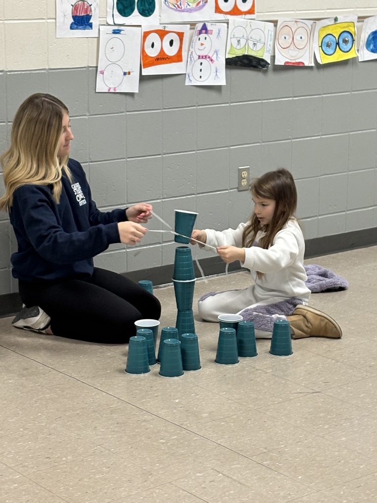 A student and child work together to stack plastic cups using a teamwork challenge involving strings.