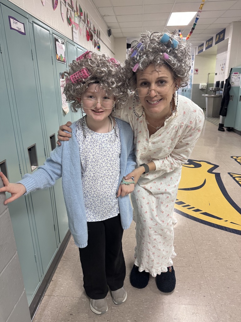 Child and adult dressed as elderly women with gray wigs and curlers in a school hallway.