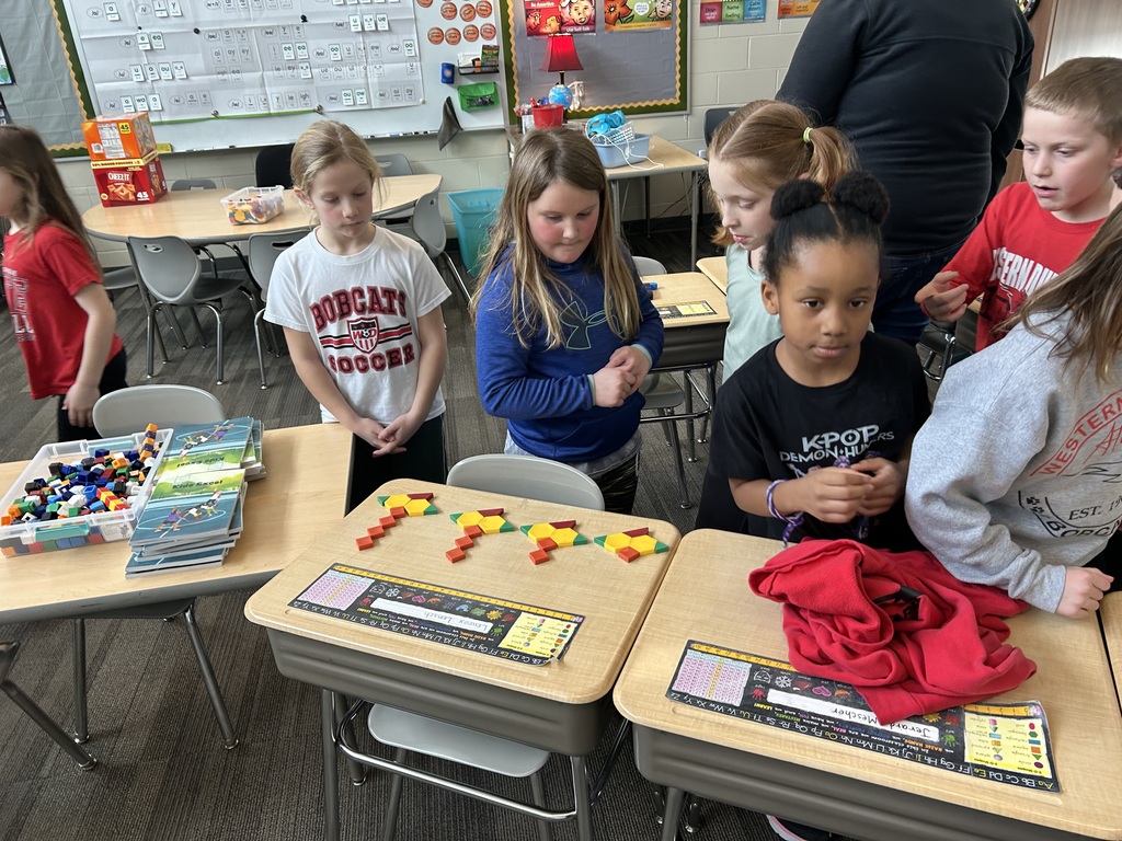 Small group of students observe geometric shapes made from pattern blocks during a classroom activity.