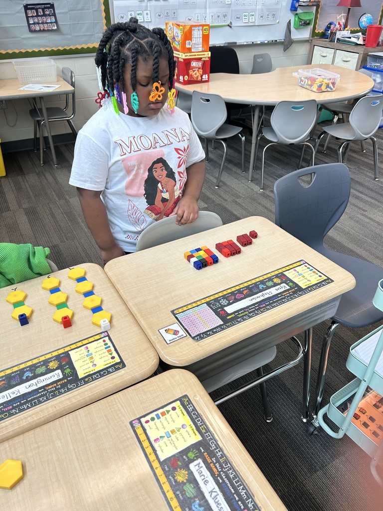 Student with colorful hair clips builds number models using linking cubes at her classroom desk.