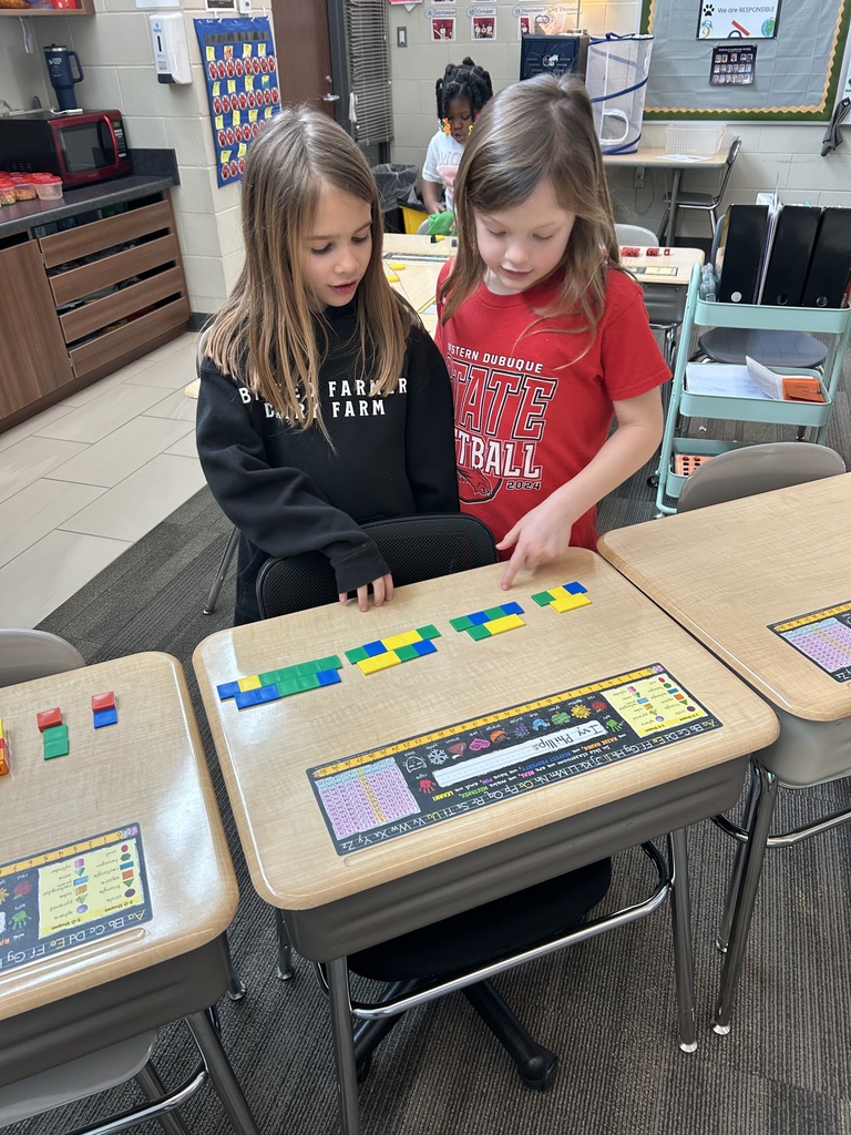Two students collaborate, arranging colored math tiles in repeating patterns on their desks.