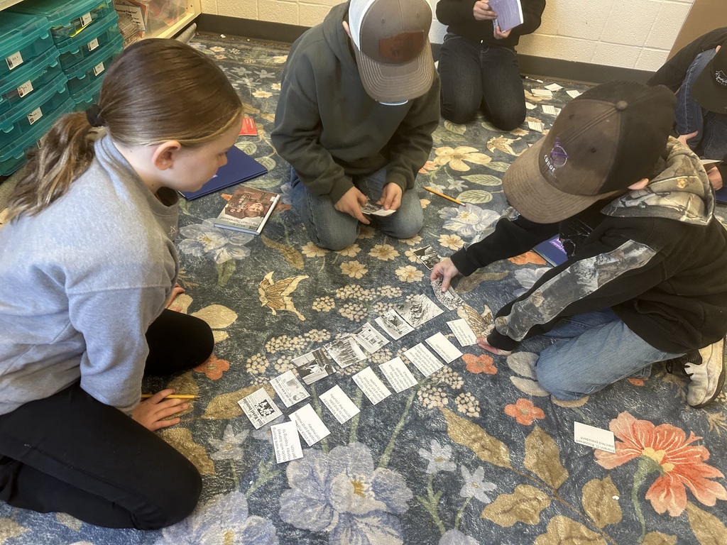 Small group of students kneel on the rug, organizing historical event cards into a chronological timeline.
