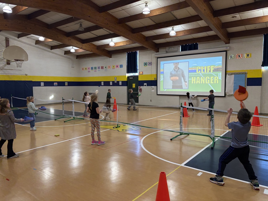 Children move around cones and nets, practicing paddle skills during an active PE class.