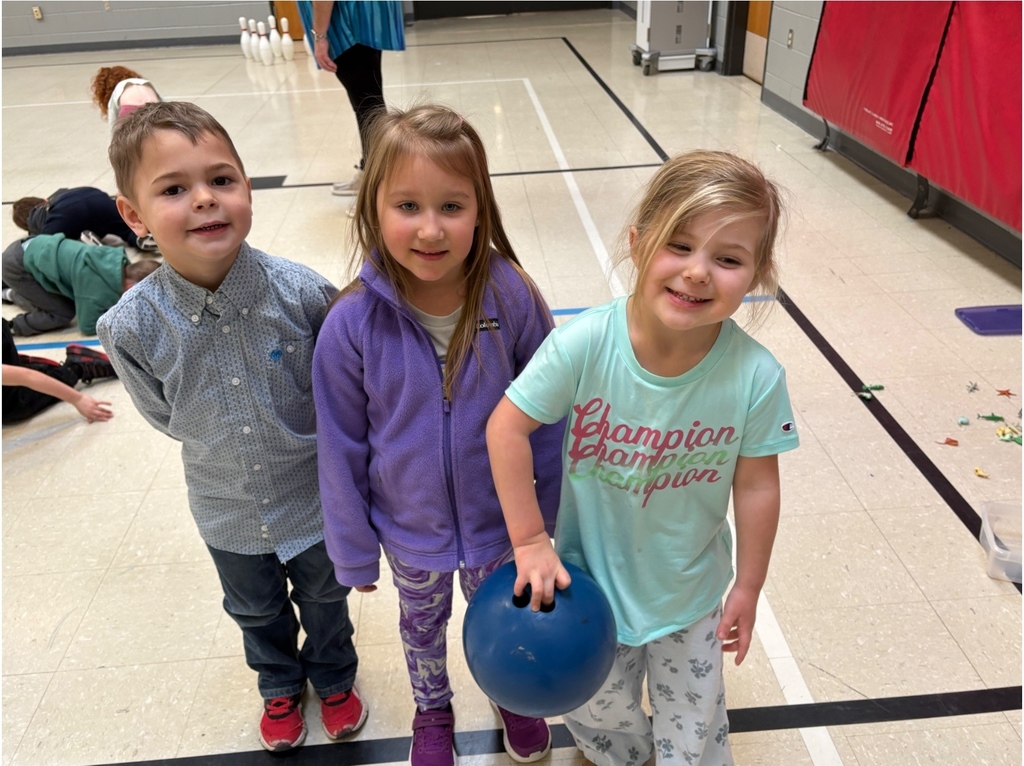 Three smiling students pose with a blue bowling ball during a bowling activity.