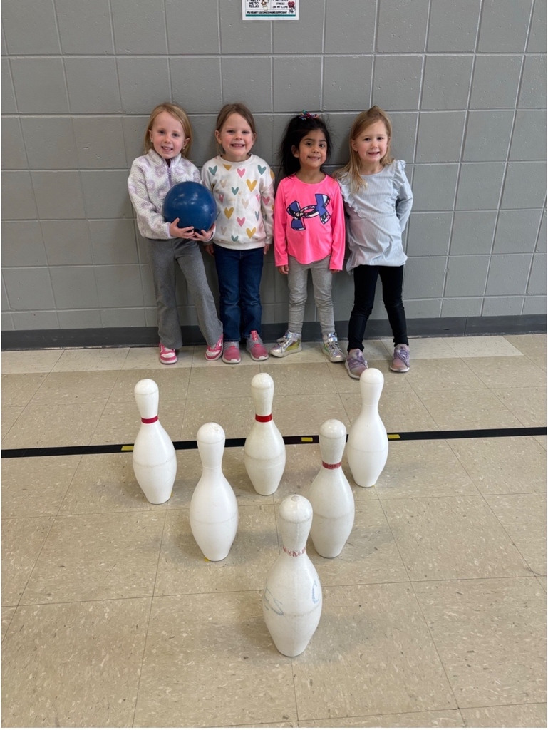 Four students stand against a wall behind a set of bowling pins, smiling after their turn.