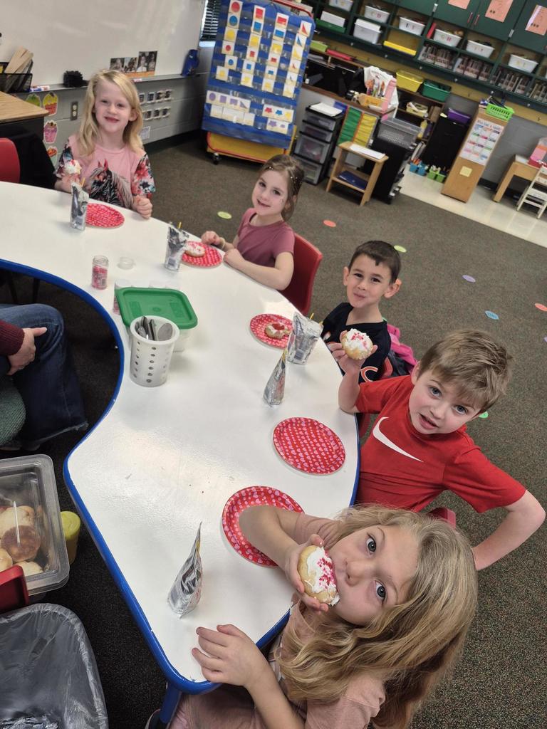 Children seated at a classroom table eating decorated cookies and drinking juice boxes.