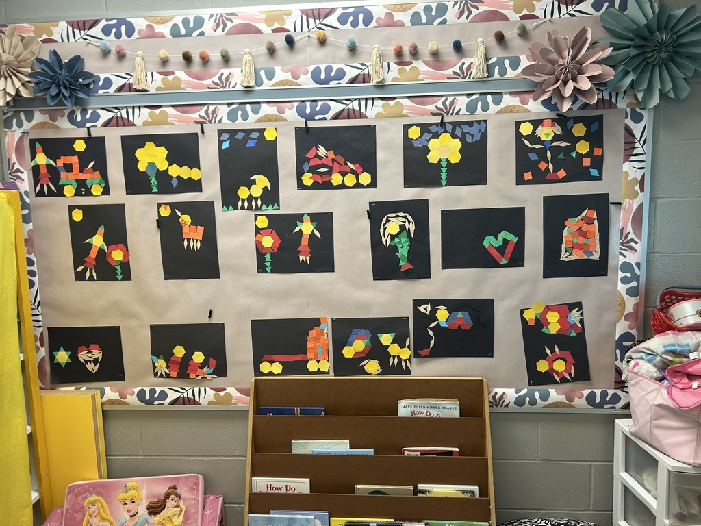 Classroom bulletin board displays colorful geometric collage artwork made from paper shapes on black backgrounds.
