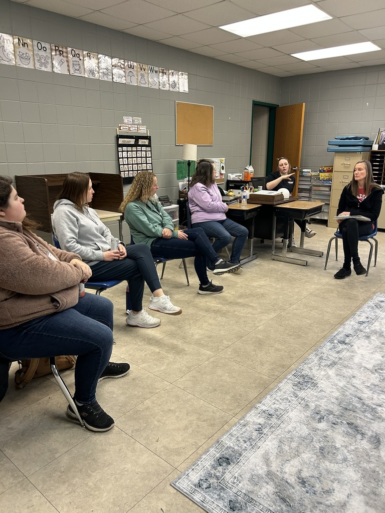 Educators sit in a circle inside a classroom while discussing ideas during a collaborative meeting.