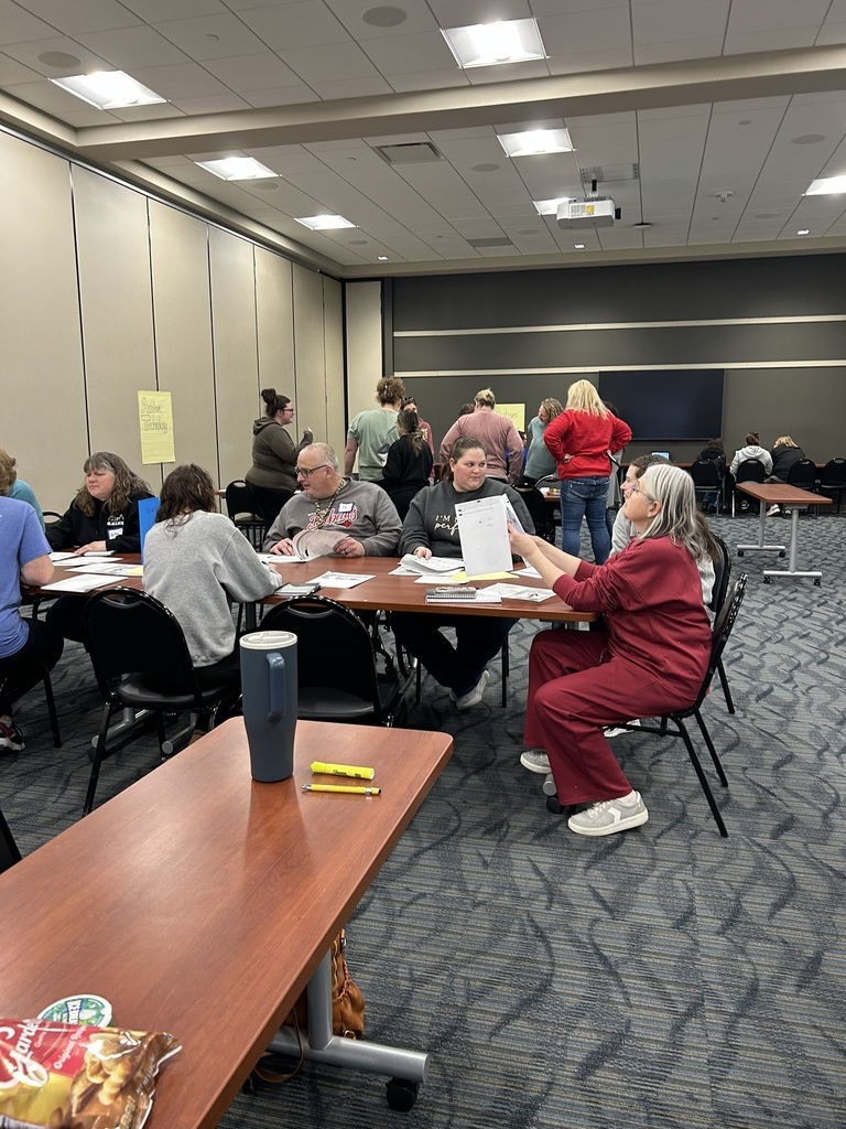 Staff members collaborate in small groups at tables while reviewing papers during a professional learning session.