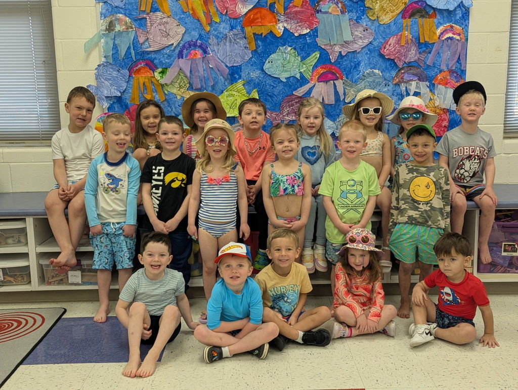 A class of preschool students dressed in beachwear and sunglasses pose together for a summer-themed classroom photo.