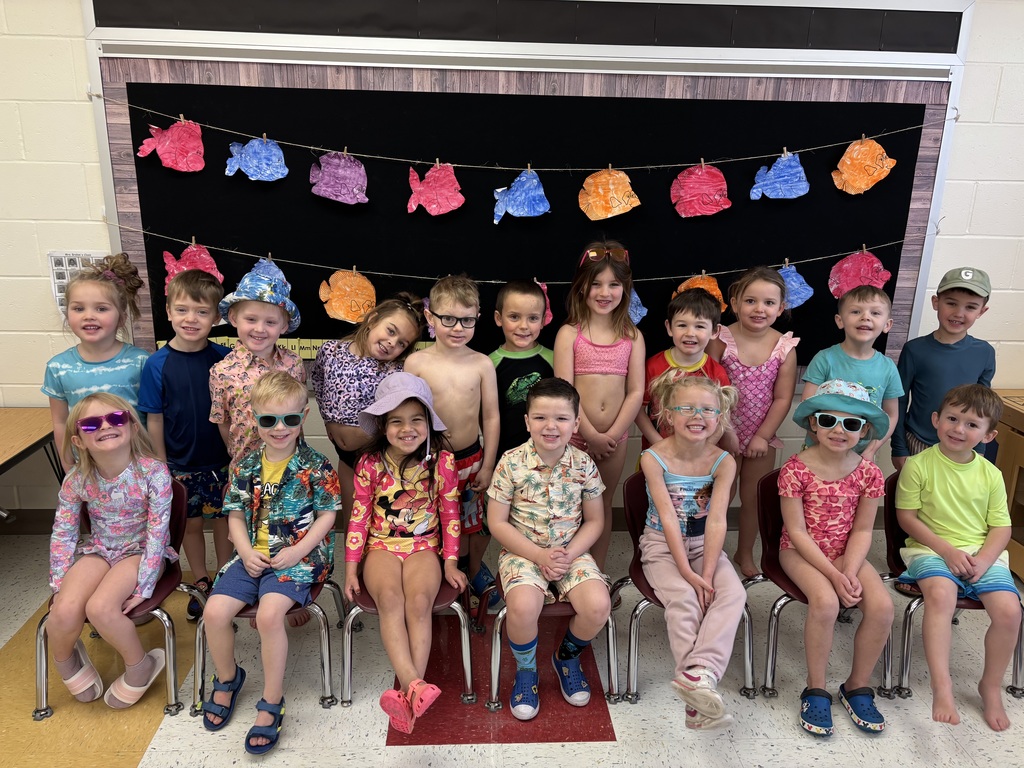 A class of preschool students dressed in beachwear and sunglasses pose together for a summer-themed classroom photo.