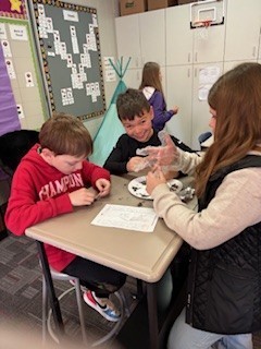 24e24b6f-e02f-4f16-815e-6171d274ba47Three students sit at a desk wearing gloves as they explore soil samples and complete a worksheet during a classroom investigation. - Kayla Wilson