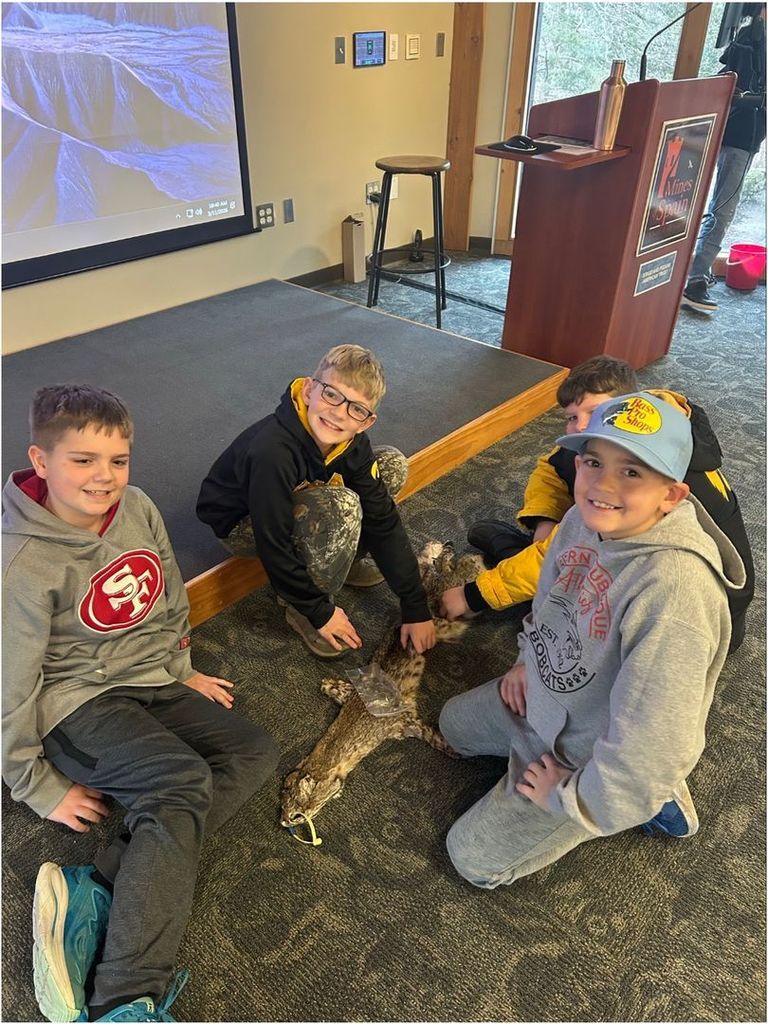 Four students kneel around an animal pelt on the floor, smiling and exploring the specimen during a hands-on learning activity.