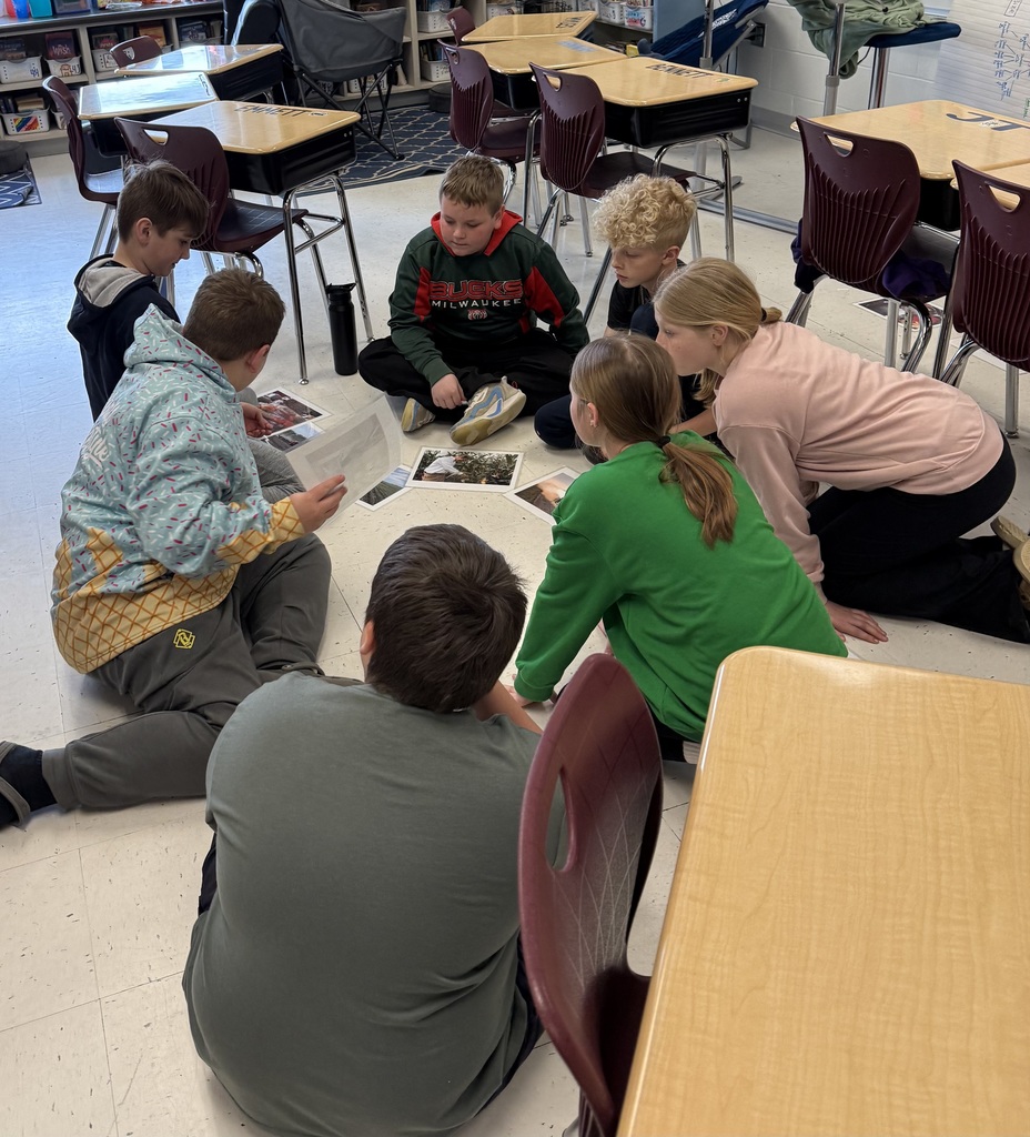 Seven students sit in a circle on the floor, examining and discussing printed images together.