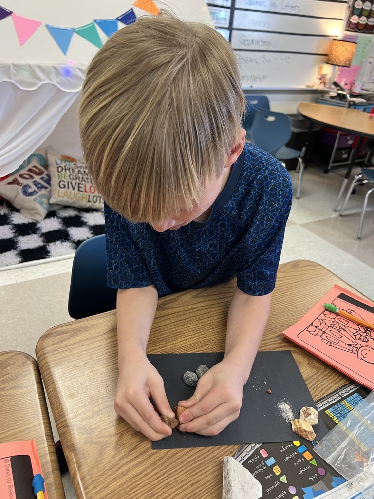 Student leans over desk, closely inspecting and breaking apart a rock sample during a hands-on science activity.