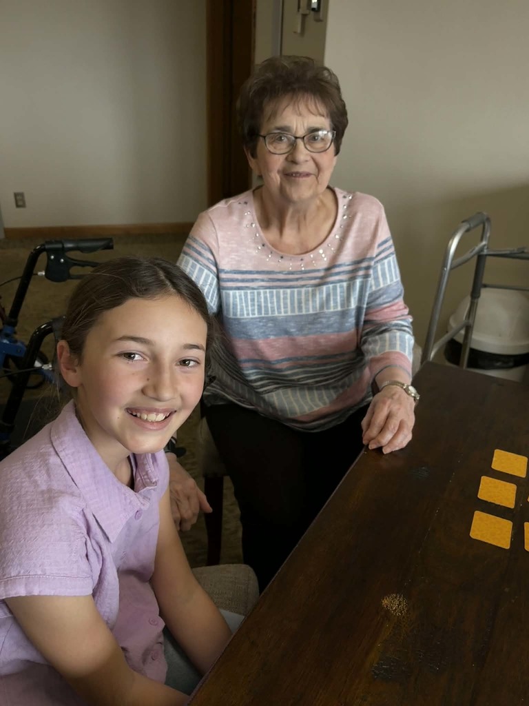 Smiling girl and older woman sit at a table with small cards, enjoying a quiet game in a care home setting.