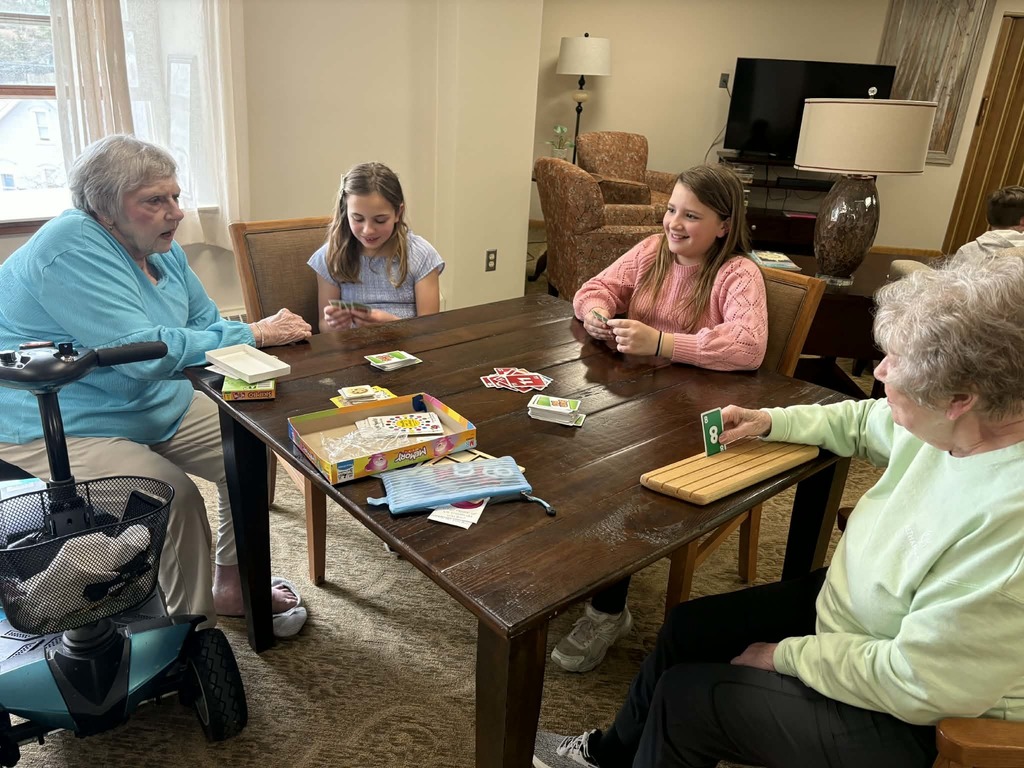 Two girls and two elderly women sit around a table playing a card game, engaged and smiling together.