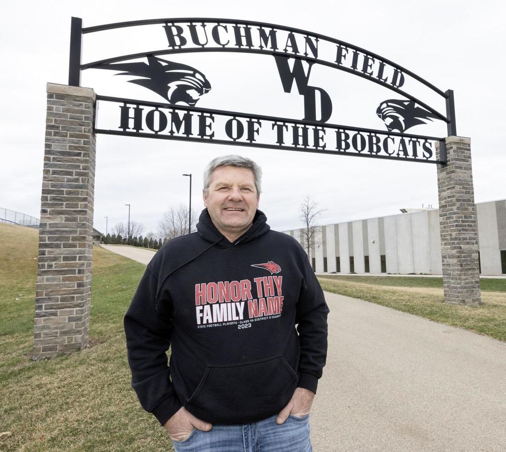 Man in a black sweatshirt standing in front of a "Home of the Bobcats" arch.