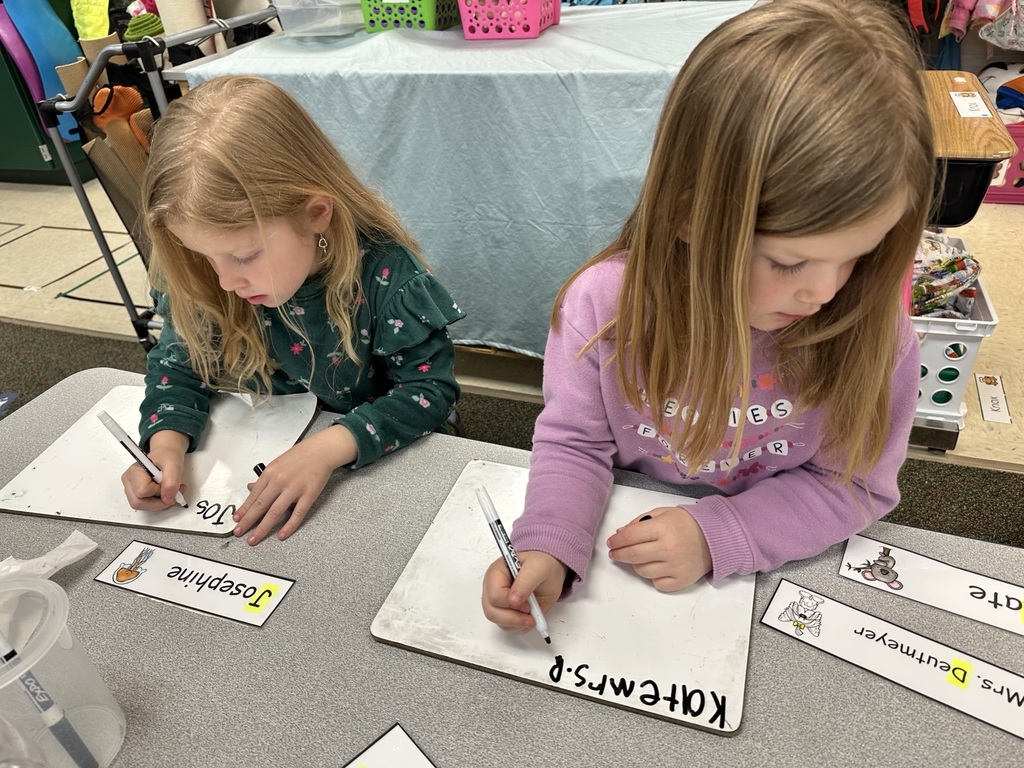 Two girls practicing writing on a markerboard.