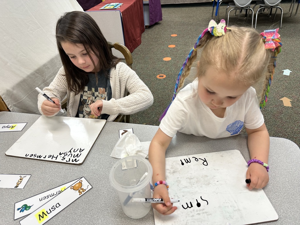 Two girls practicing writing on a markerboard.