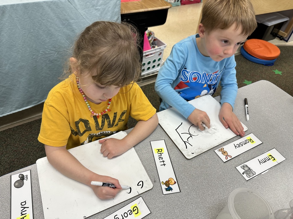 Two children practicing writing on a markerboard.