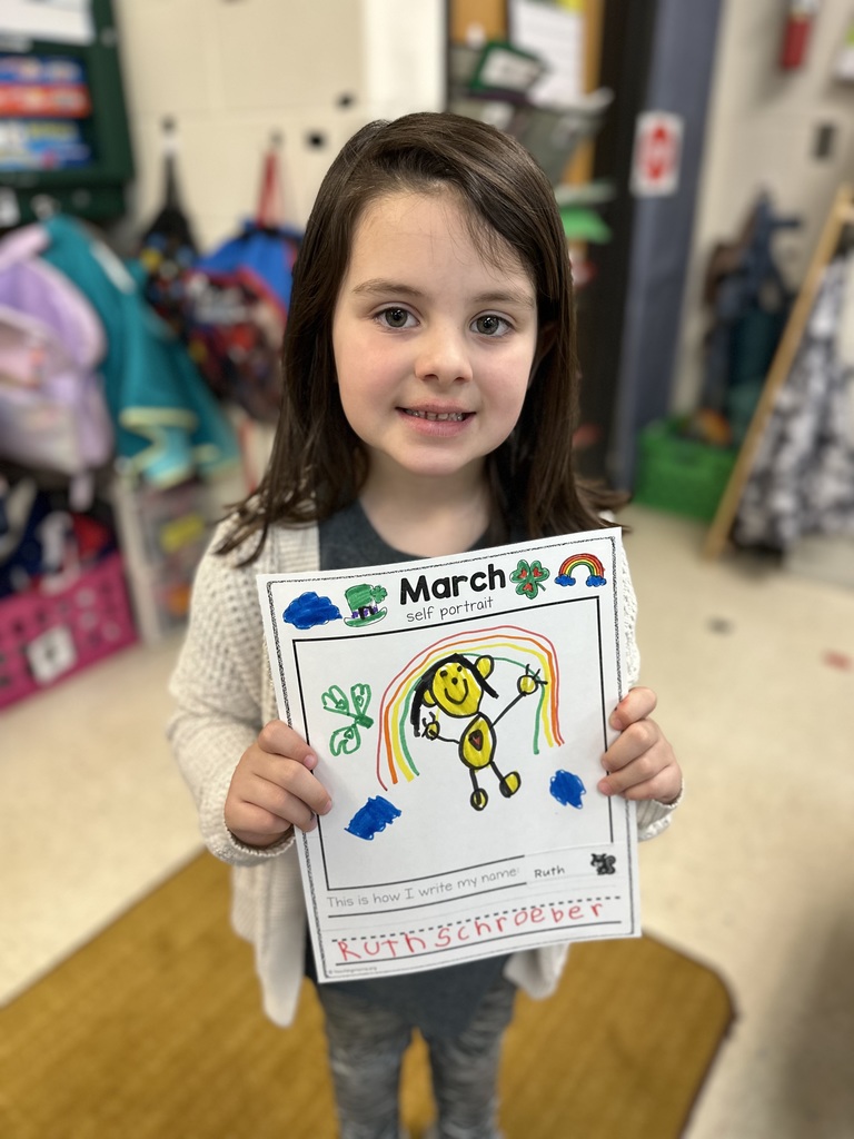 A young girl holding up a drawing of herself.