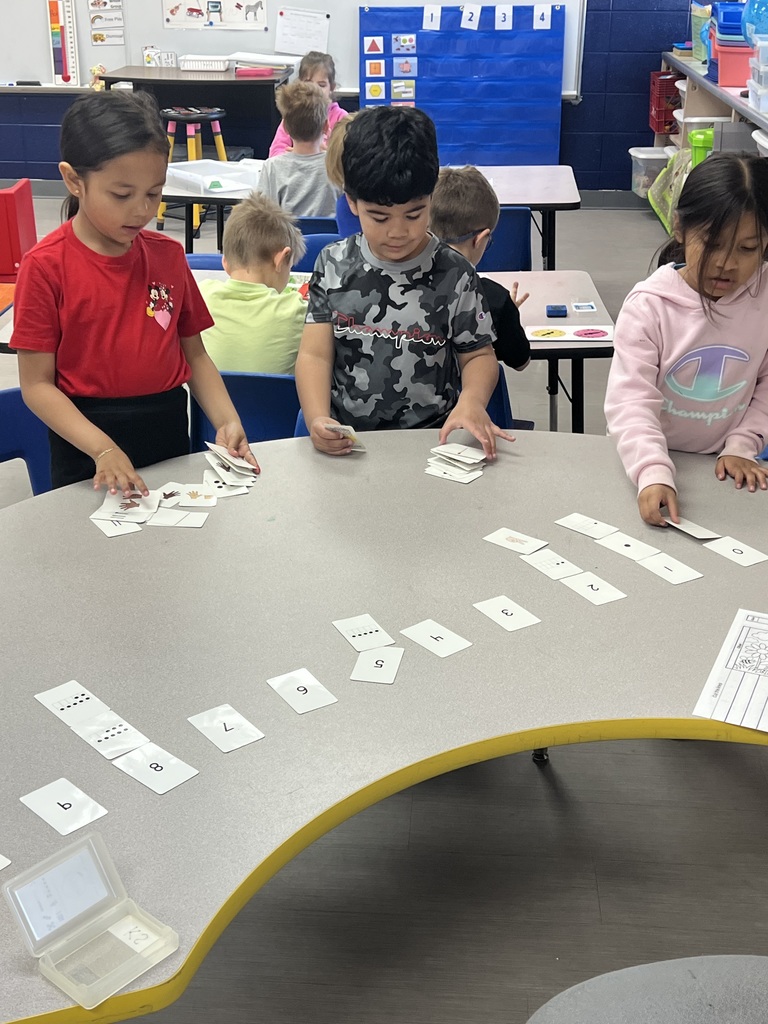 Three students looking at table with cards that have dots and numbers on them.