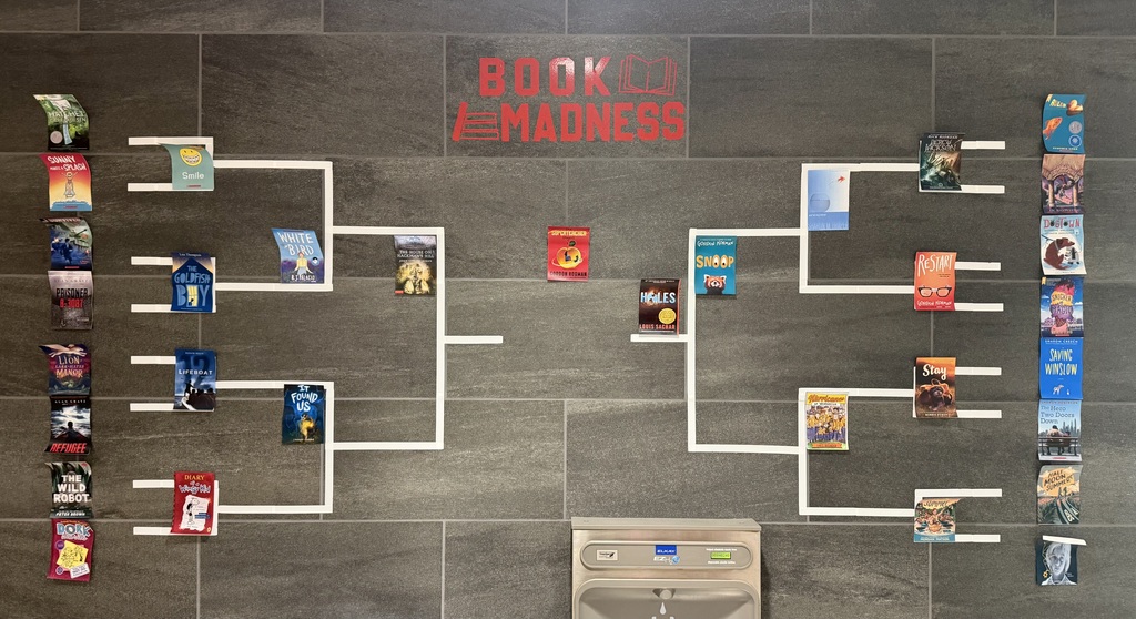 Wall display titled “Book Madness” shows a tournament bracket with book covers arranged in matchups above a drinking fountain.