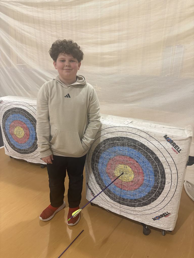 Boy in gray hoodie stands next to target with an arrow in the bullseye.