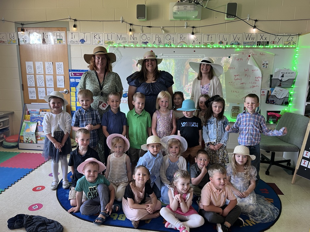 Kindergarten students and teachers dressed in spring hats enjoy a classroom tea party with snacks, tea cups, and colorful decorations.