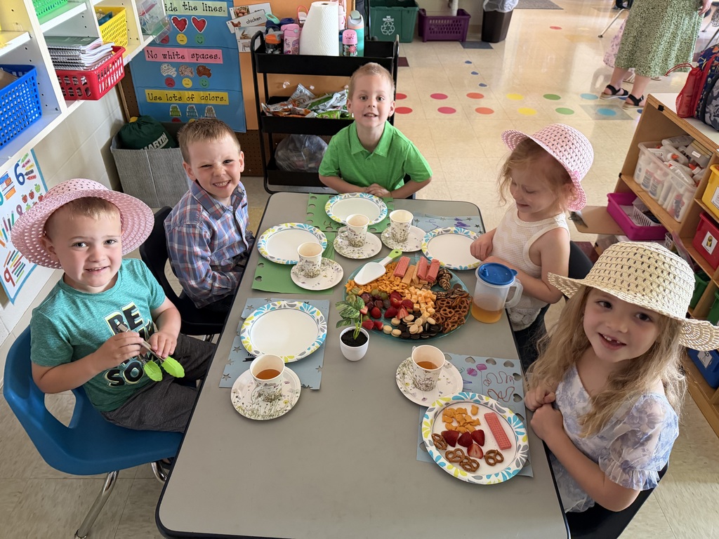 Kindergarten students and teachers dressed in spring hats enjoy a classroom tea party with snacks, tea cups, and colorful decorations.