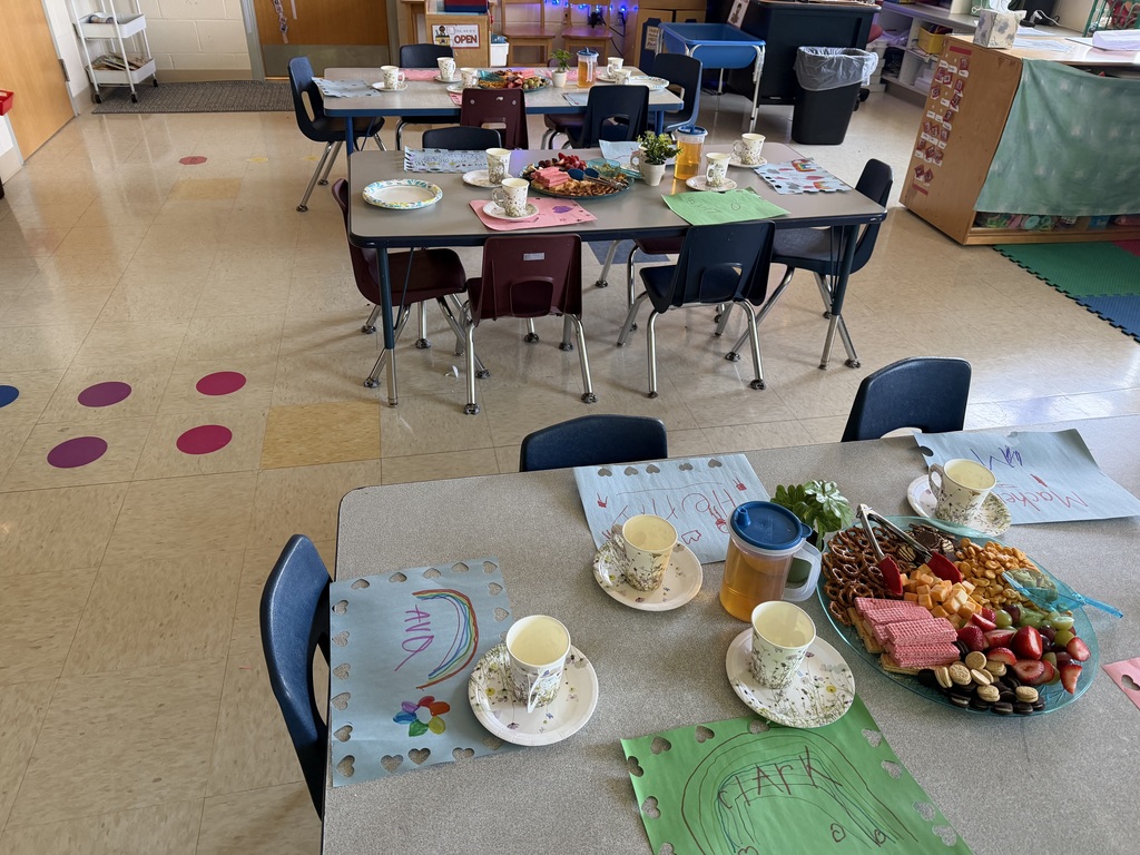 Kindergarten students and teachers dressed in spring hats enjoy a classroom tea party with snacks, tea cups, and colorful decorations.