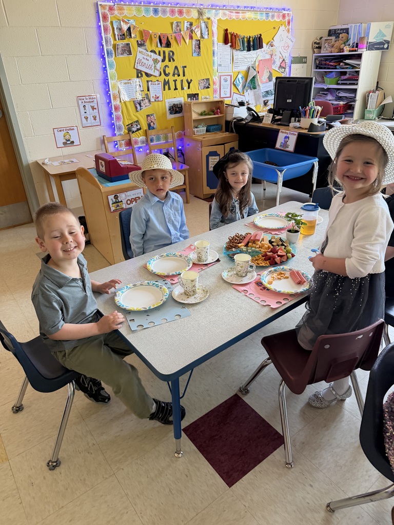 Kindergarten students and teachers dressed in spring hats enjoy a classroom tea party with snacks, tea cups, and colorful decorations.